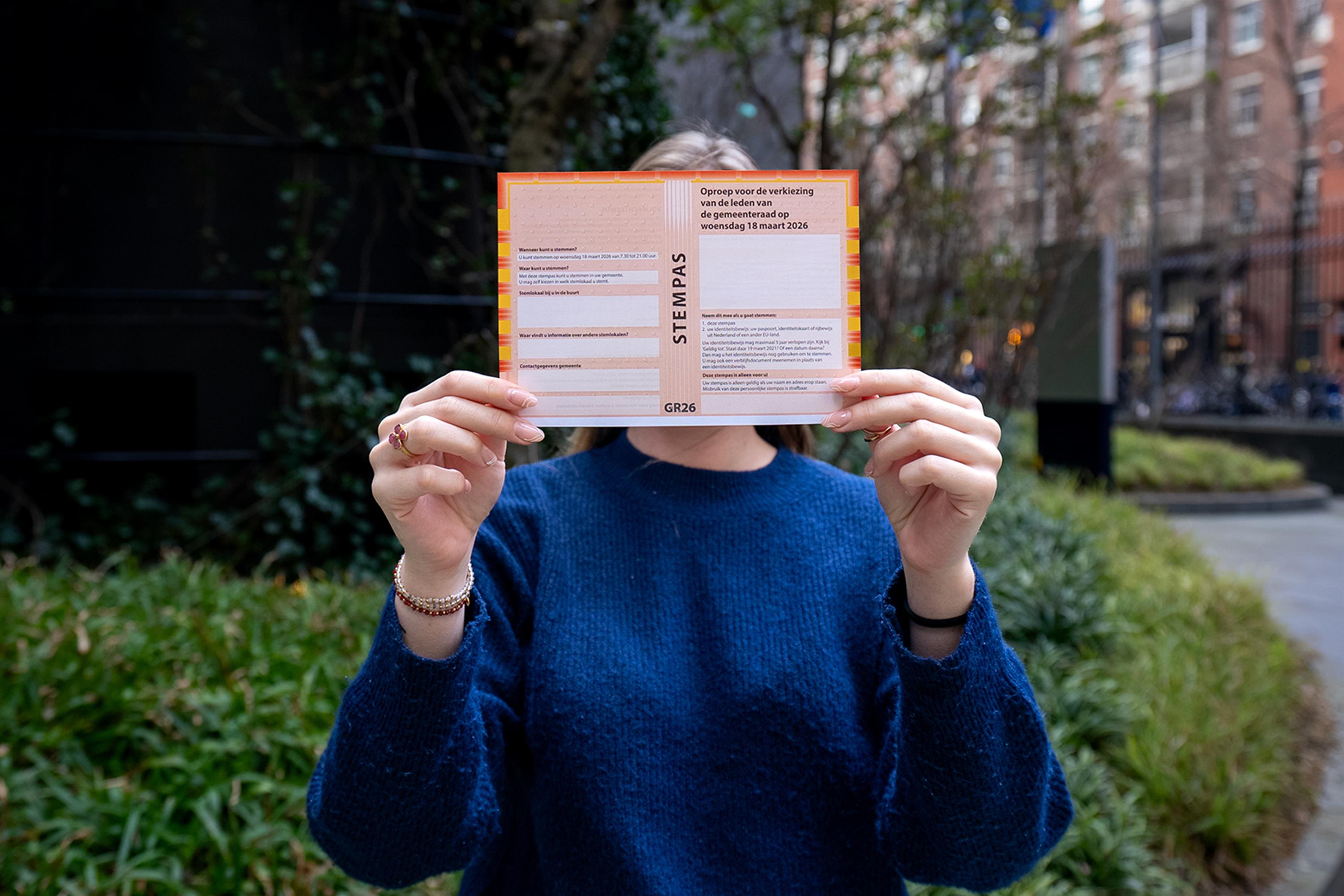 Foto van een vrouw die een stempas voor de gemeenteraadsverkiezingen omhoog houdt. 