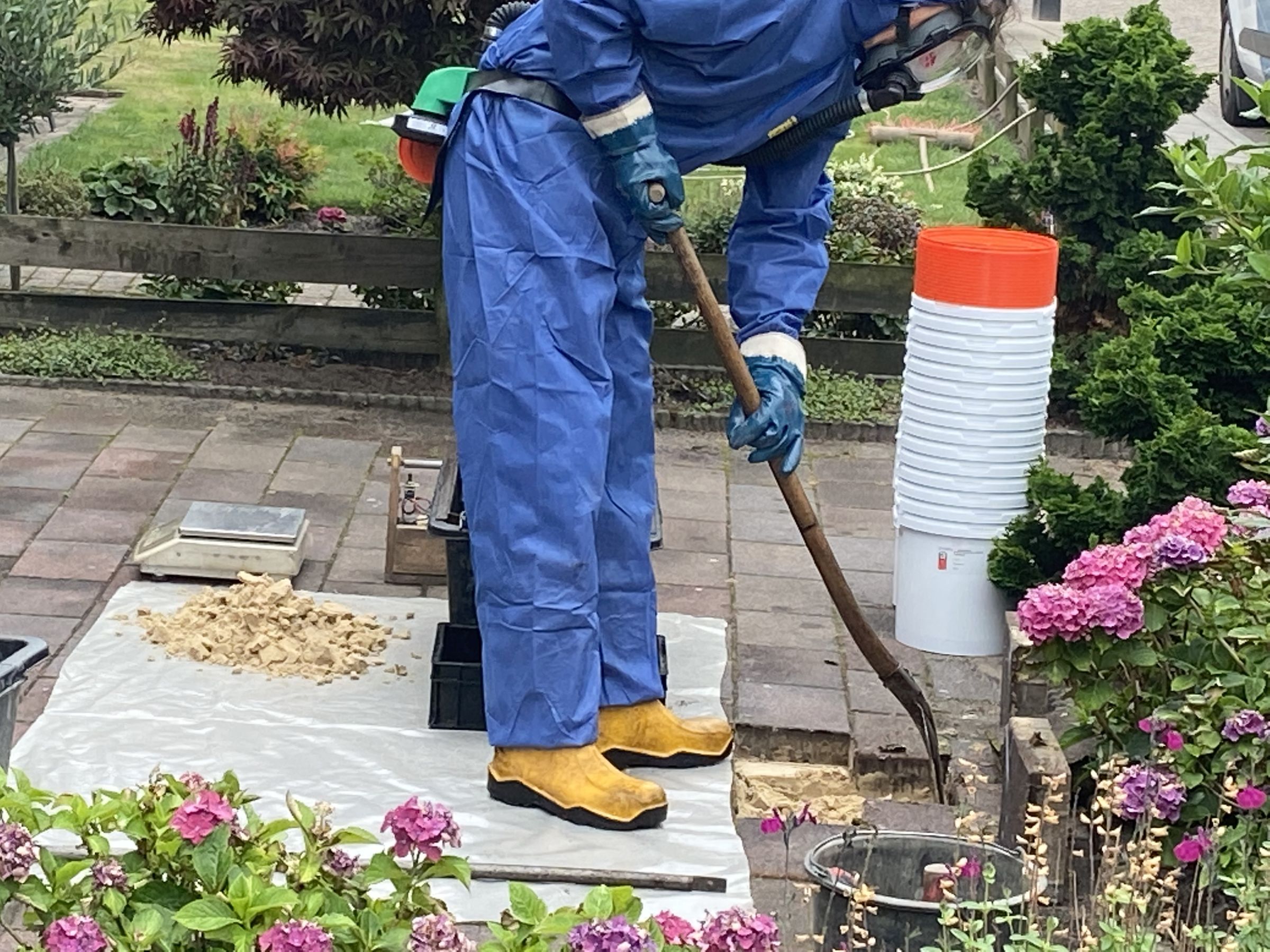 Persoon in beschermende kleding doet asbestonderzoek. Wipt een tegel uit de tuin. 