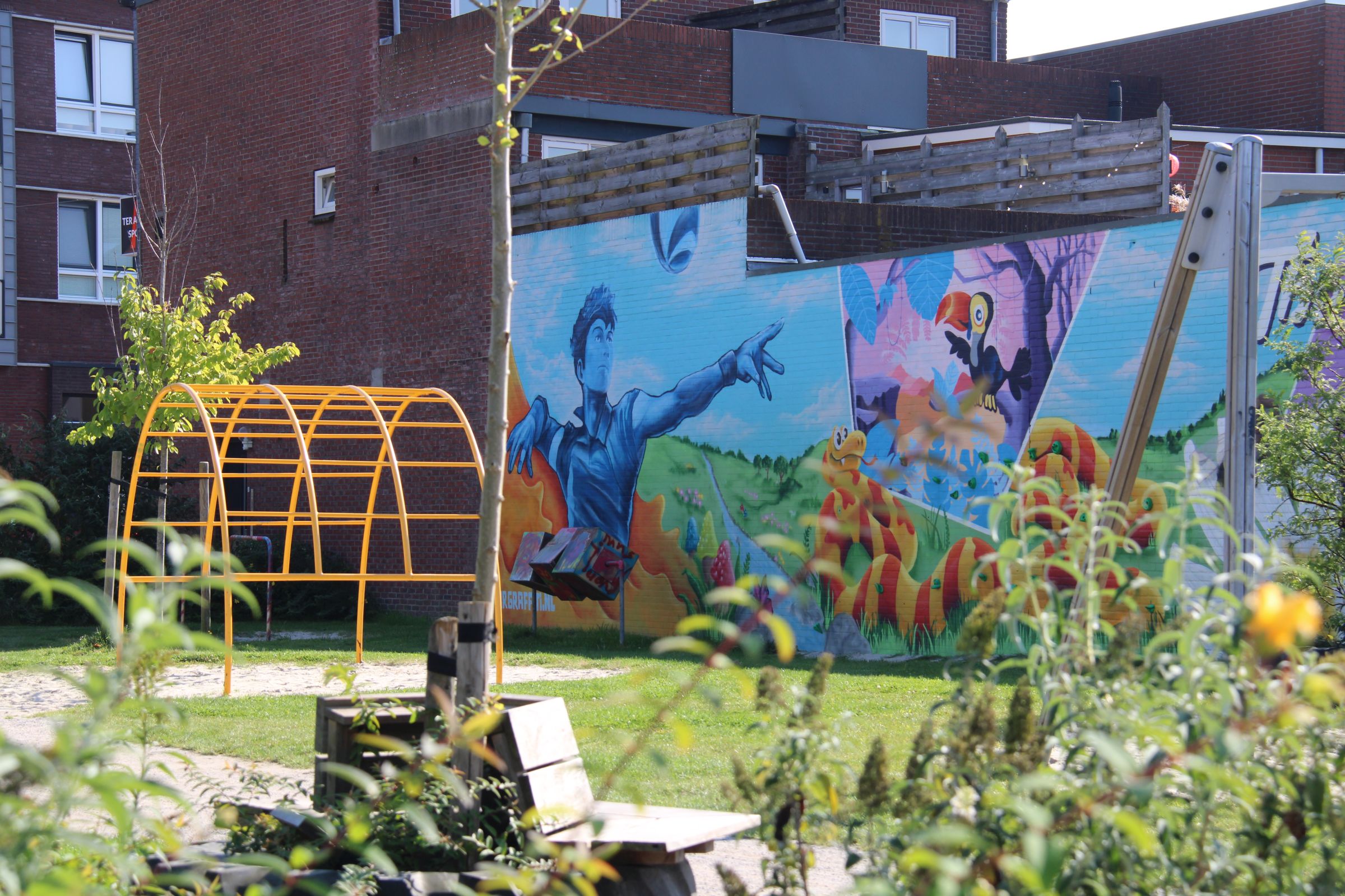 Speeltuin met bankje en struiken en op de achtergrond een muur met graffiti.
