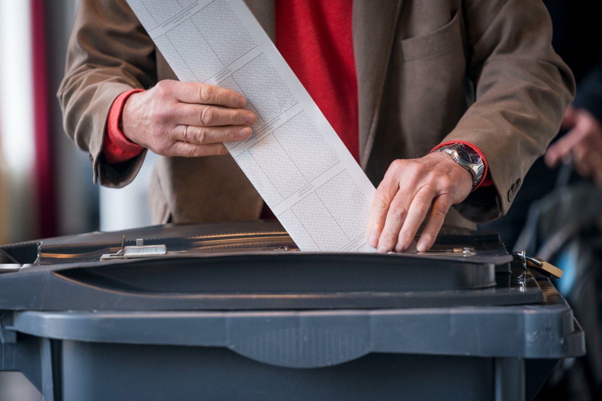 Hand van iemand die een stembiljet in een stembus doet (stockfoto).