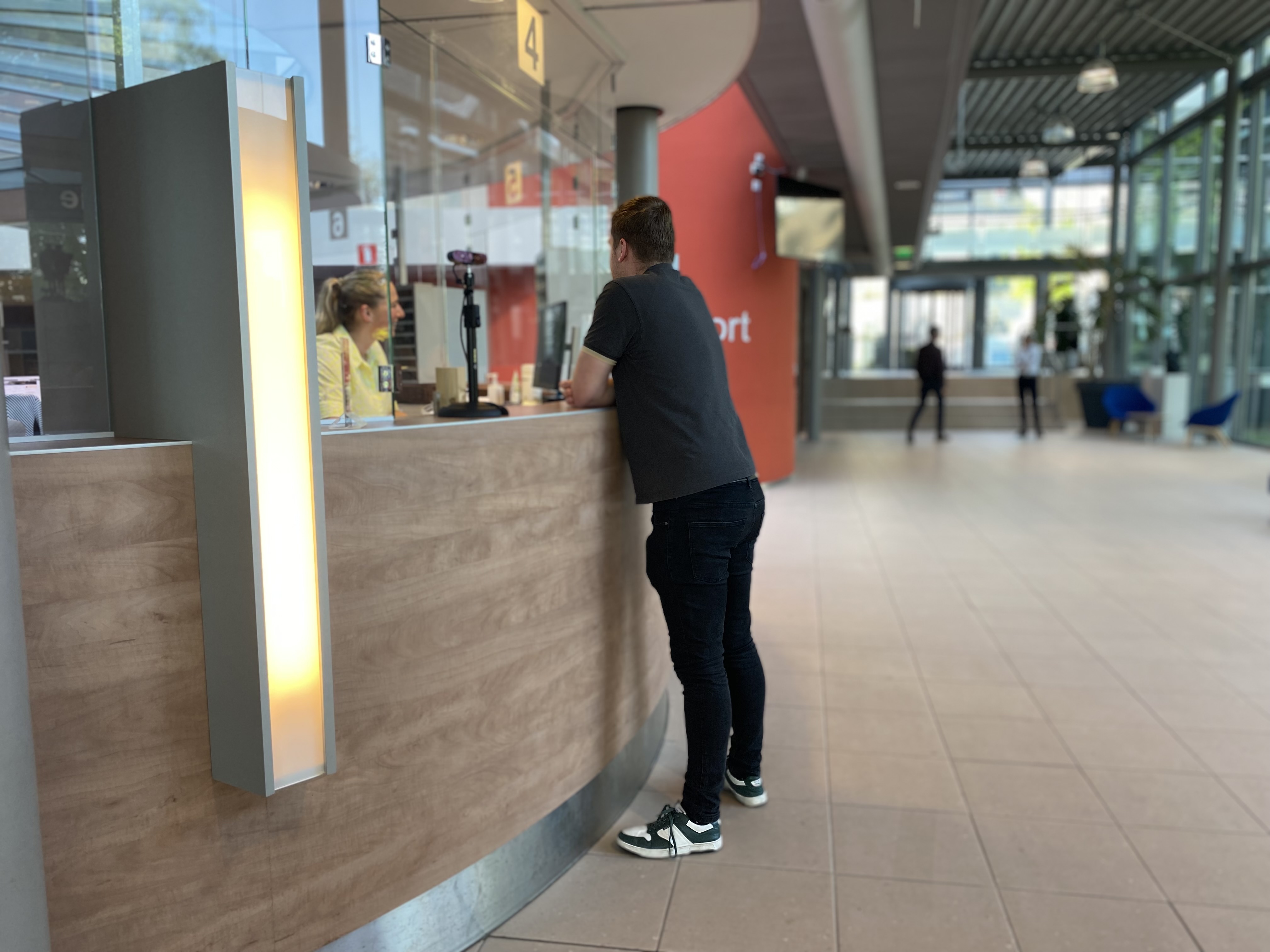 Man staat aan publieksbalie. Vrouwelijke medewerker achter de balie. 