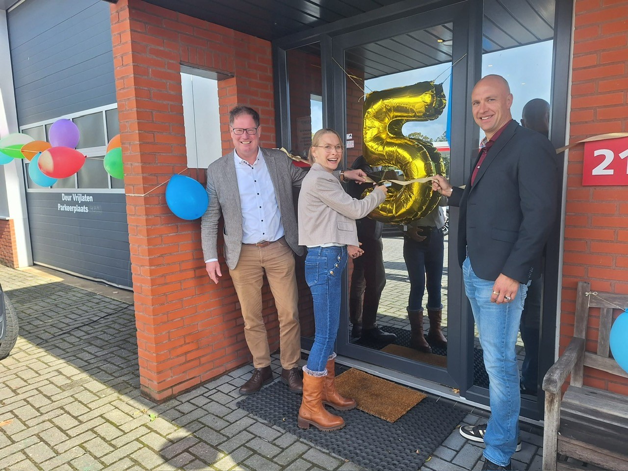 Wethouder Jan-Herman Scholten en twee mensen van Bertu Toegangstechniek bij met ballonnen versierde deur van bedrijfspand.