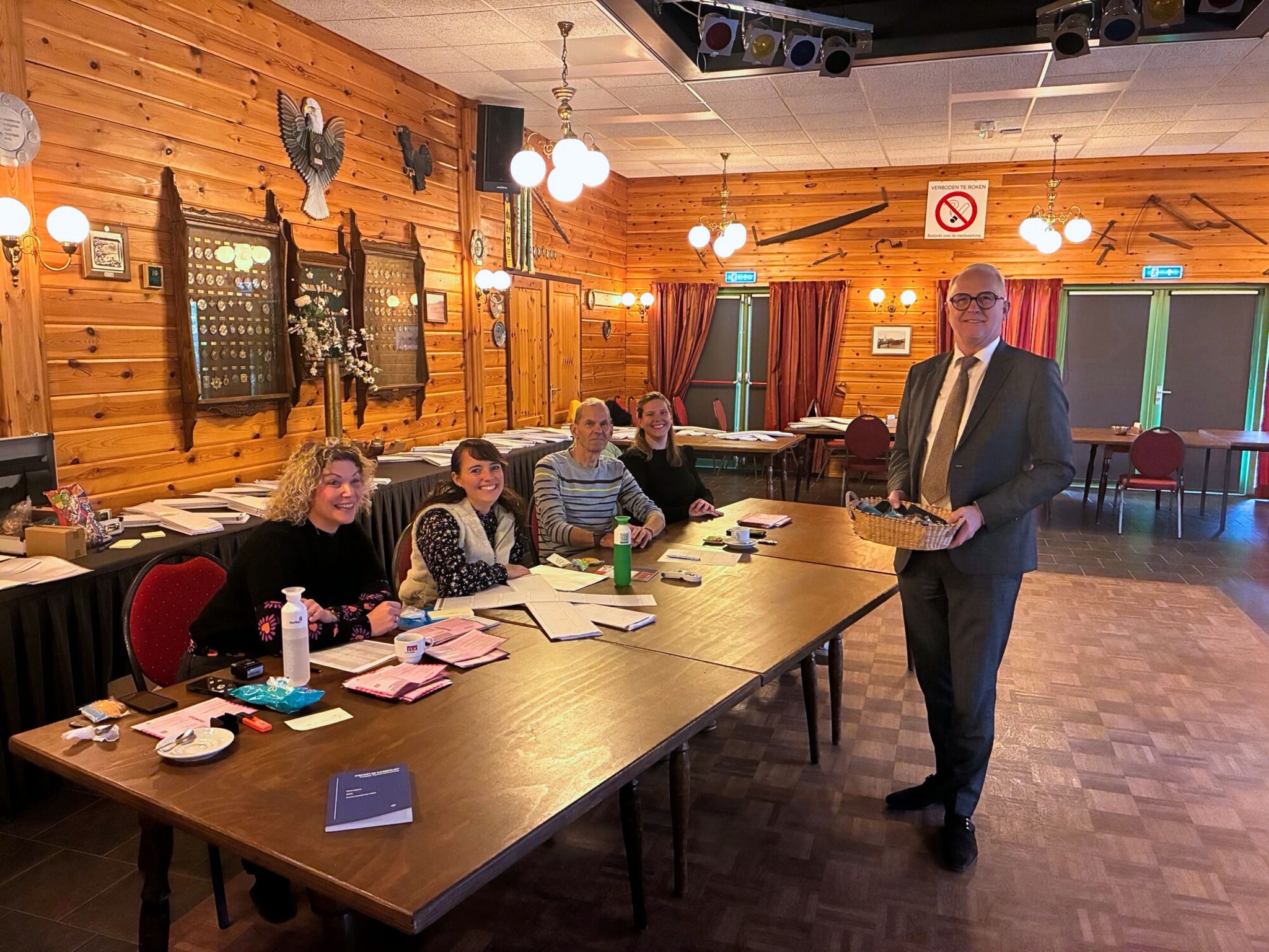 Foto van stembureau Het Schuttershoes tijden de Tweede Kamerverkiezingen. Vier stembureauleden achter een tafel en burgemeester Gerard van den Hengel op de voorgrond. 