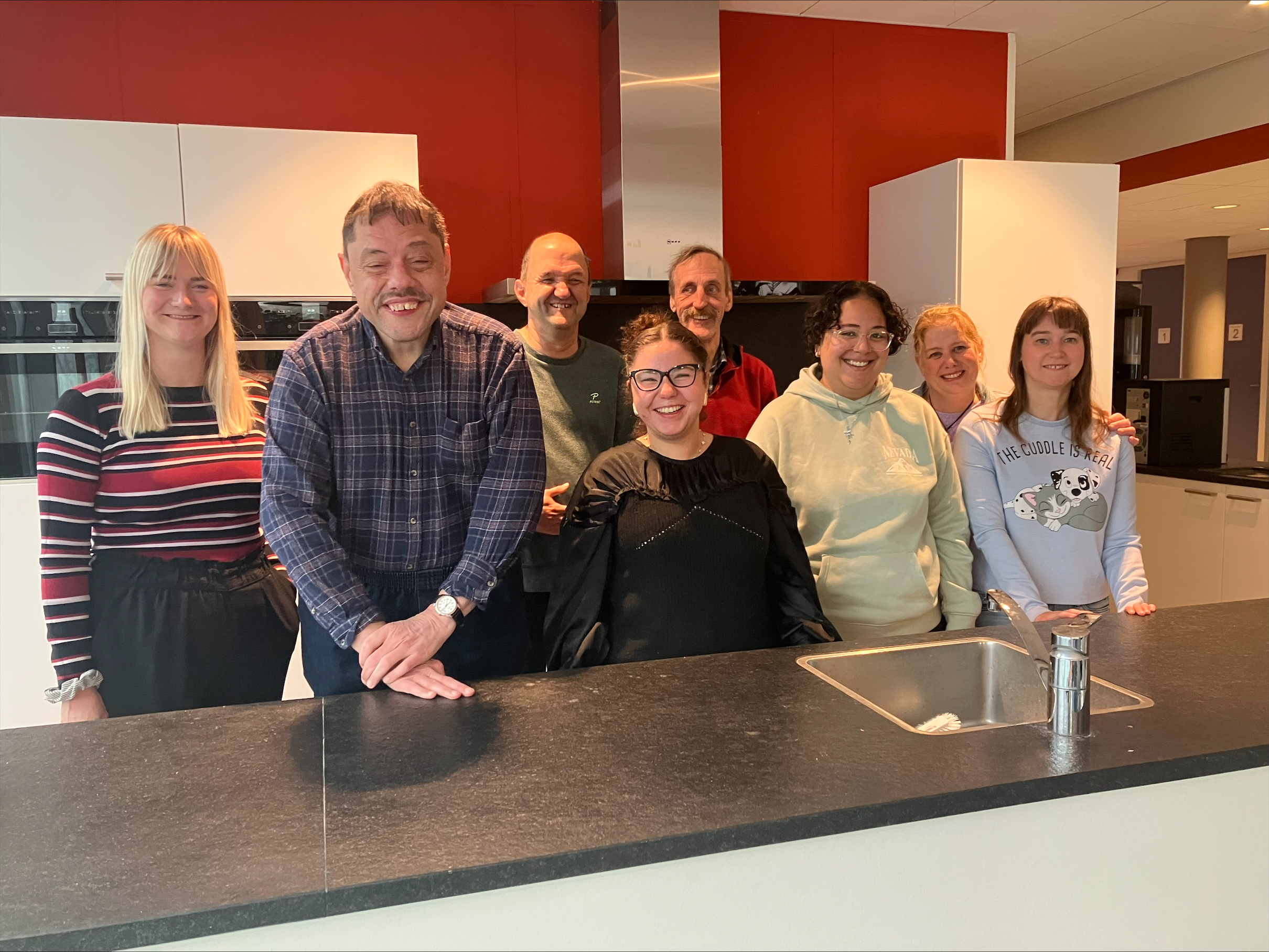 Groep cliënten van zorginstelling Aveleijn poseert met begeleiders in de keuken van de Noaberpoort. 