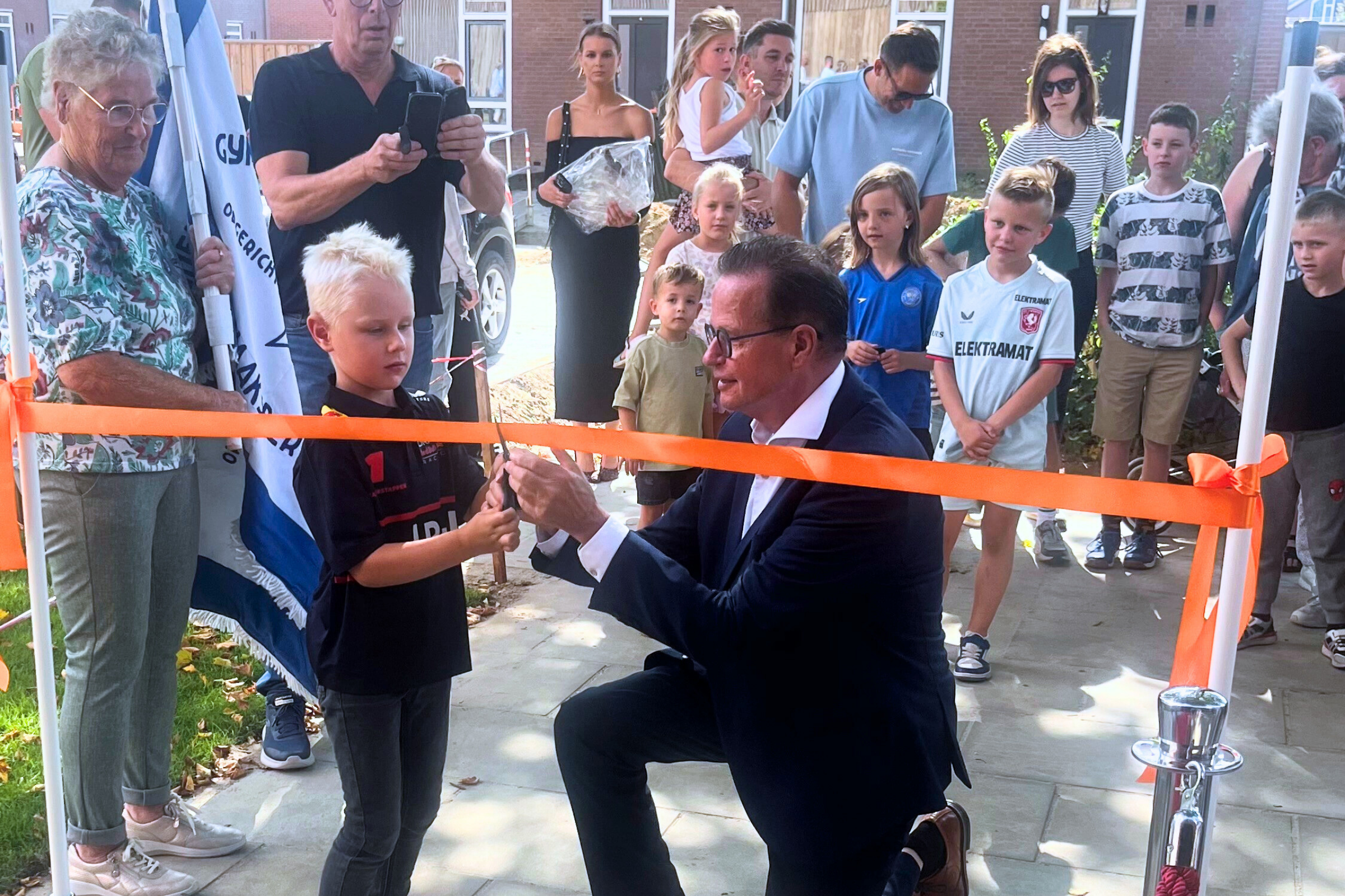 Wethouder Pieter van Zwanenburg knipt samen met een jongetje een lint door. Andere mensen kijken toe. 