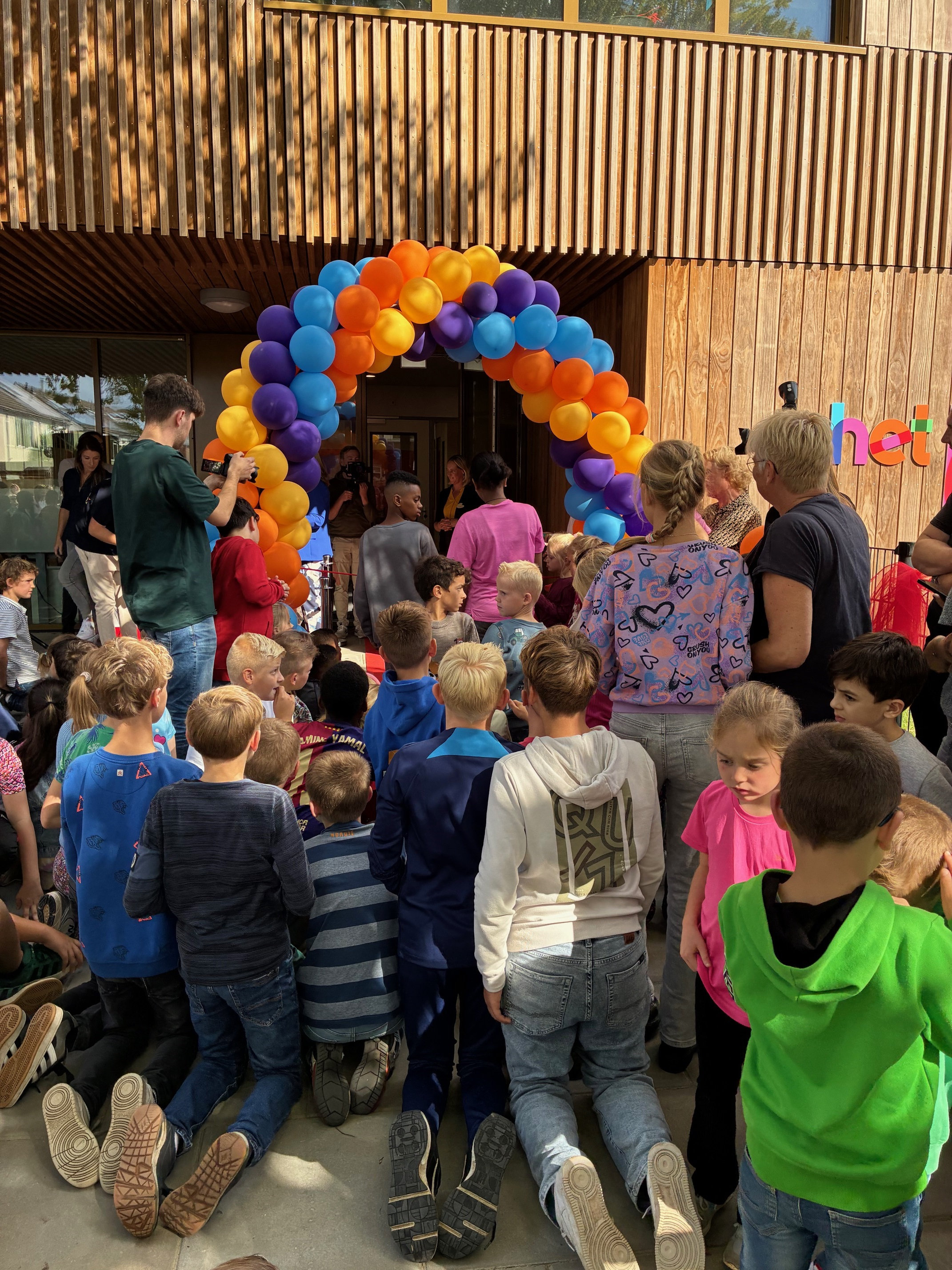 Groep kinderen bij ballonnenboog voor feestelijke opening basisschool Het Palet. 