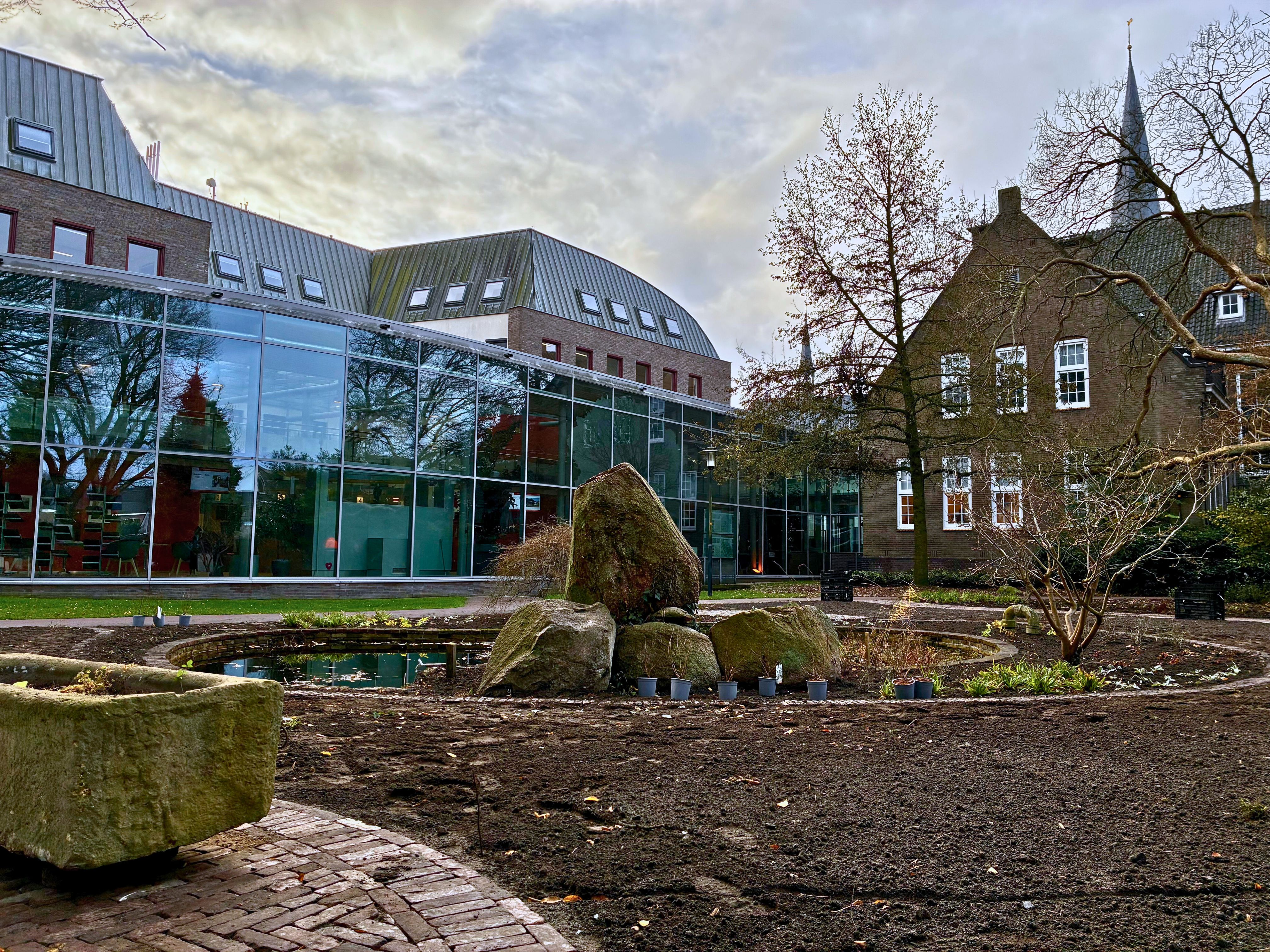 Foto van de gemeentetuin met vijver in het midden en links onderin een deel van de paardenkrik. Op de achtergrond het gemeentehuis. 