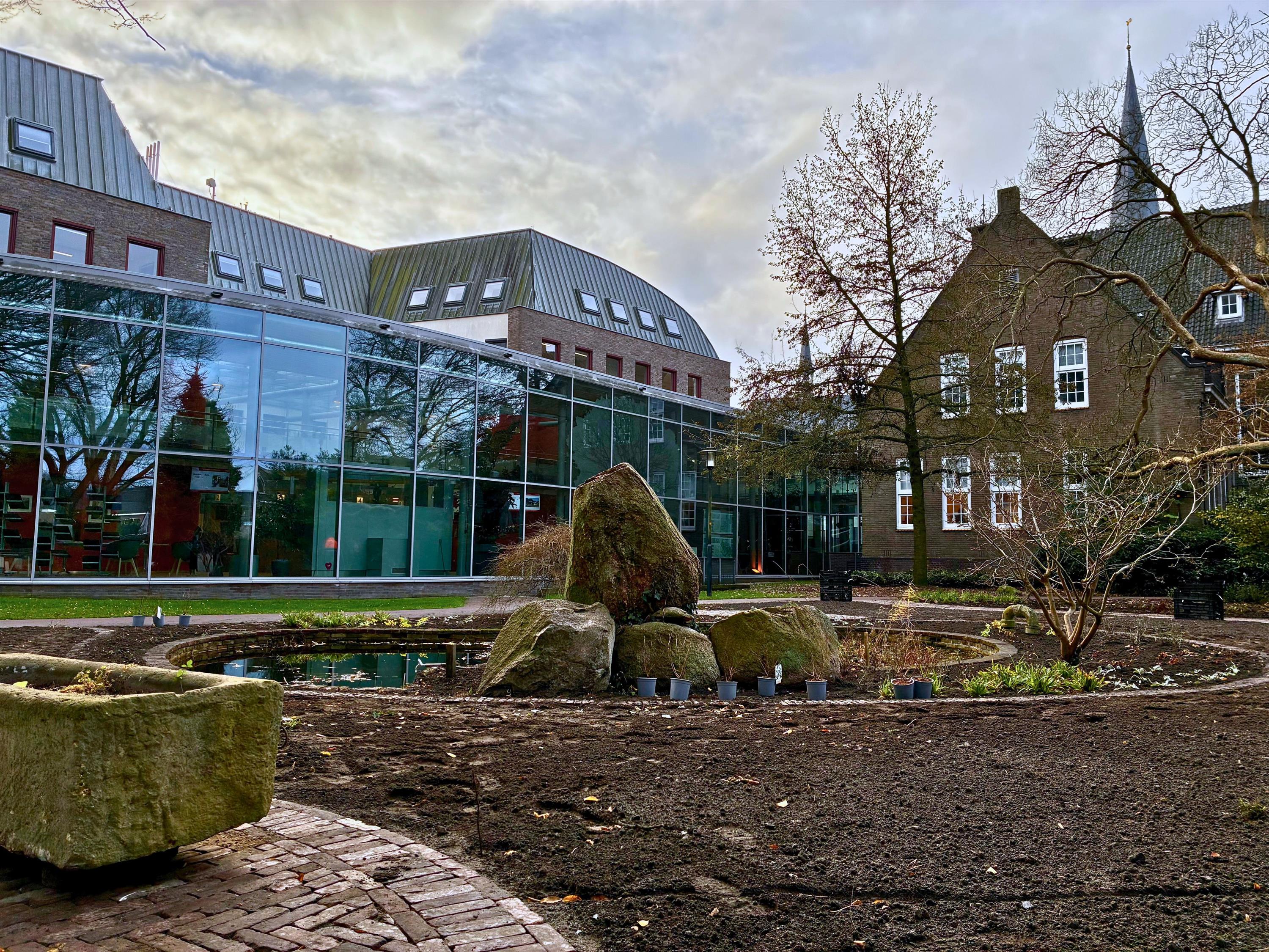 Foto van de gemeentetuin met vijver in het midden en links onderin een deel van de paardenkrik. Op de achtergrond het gemeentehuis. 