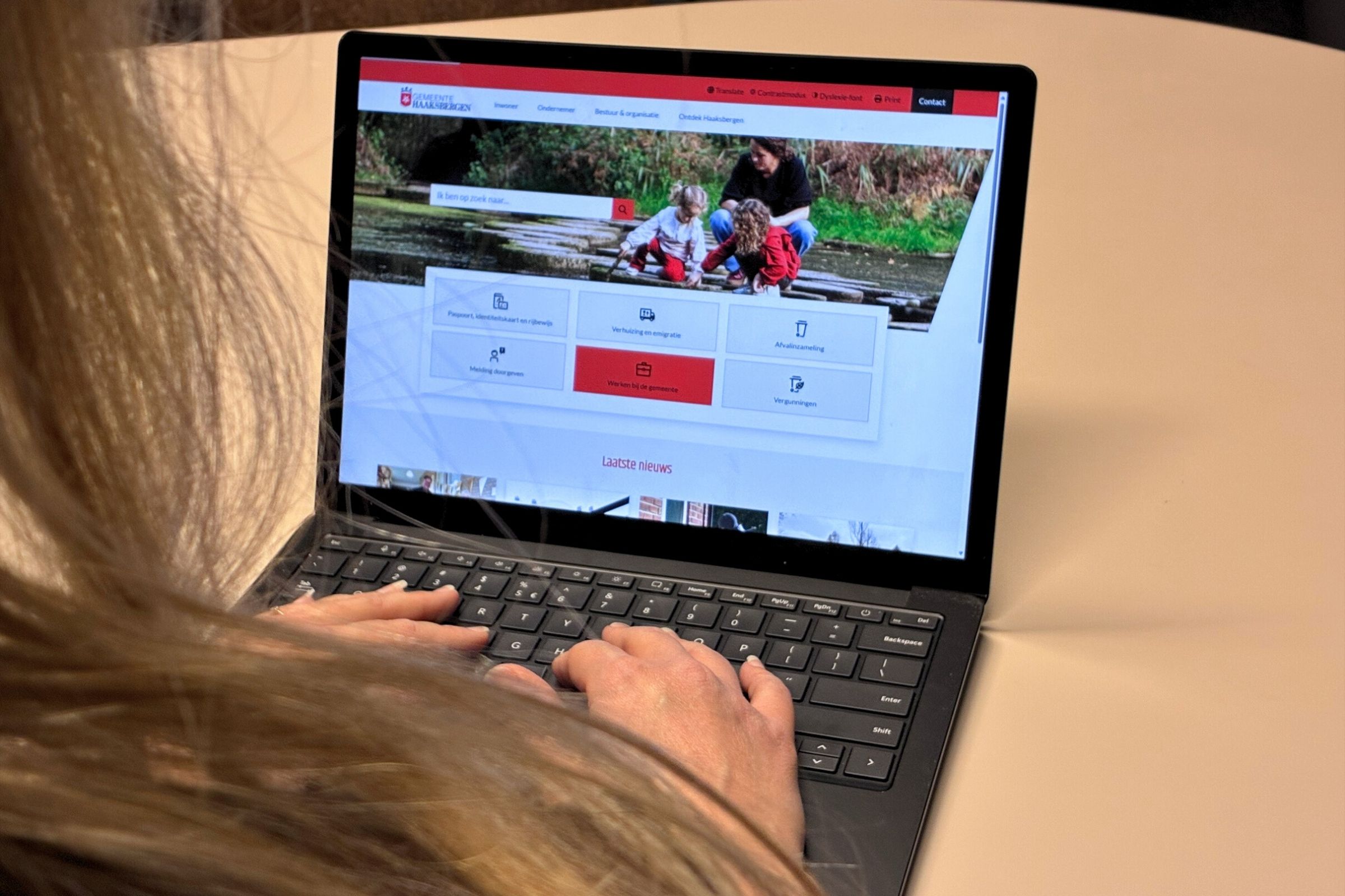 Foto van een laptop waarop de homepage van het vernieuwde haaksbergen.nl geopend is.  Je kijkt over de schouder mee bij iemand achter de laptop. 