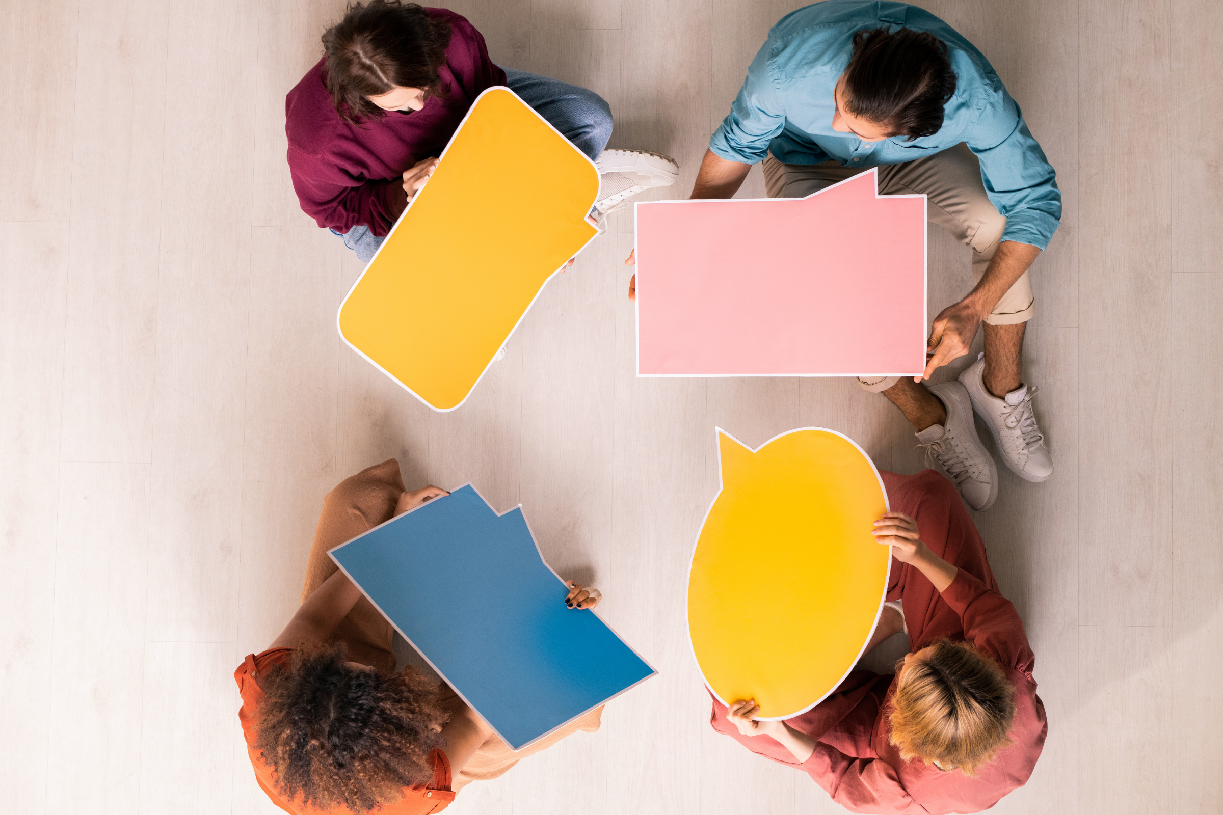 Vier mensen in een kring houden allemaal een lege tekstballon vast. Tekstballonnen in verschillende vormen.  