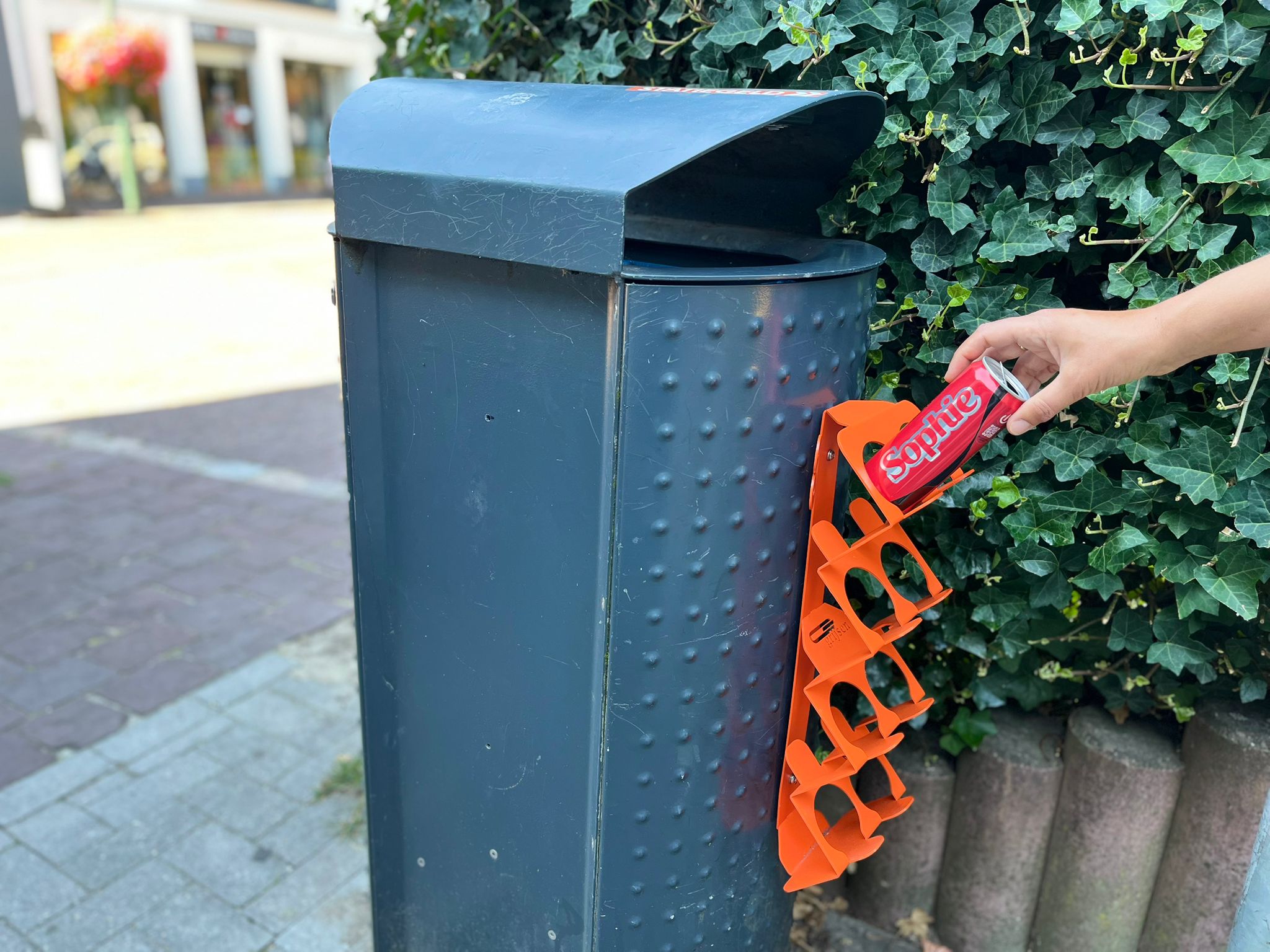 Hand plaatst een colablikje in de statiegeldbeugel aan de prullenbak. 