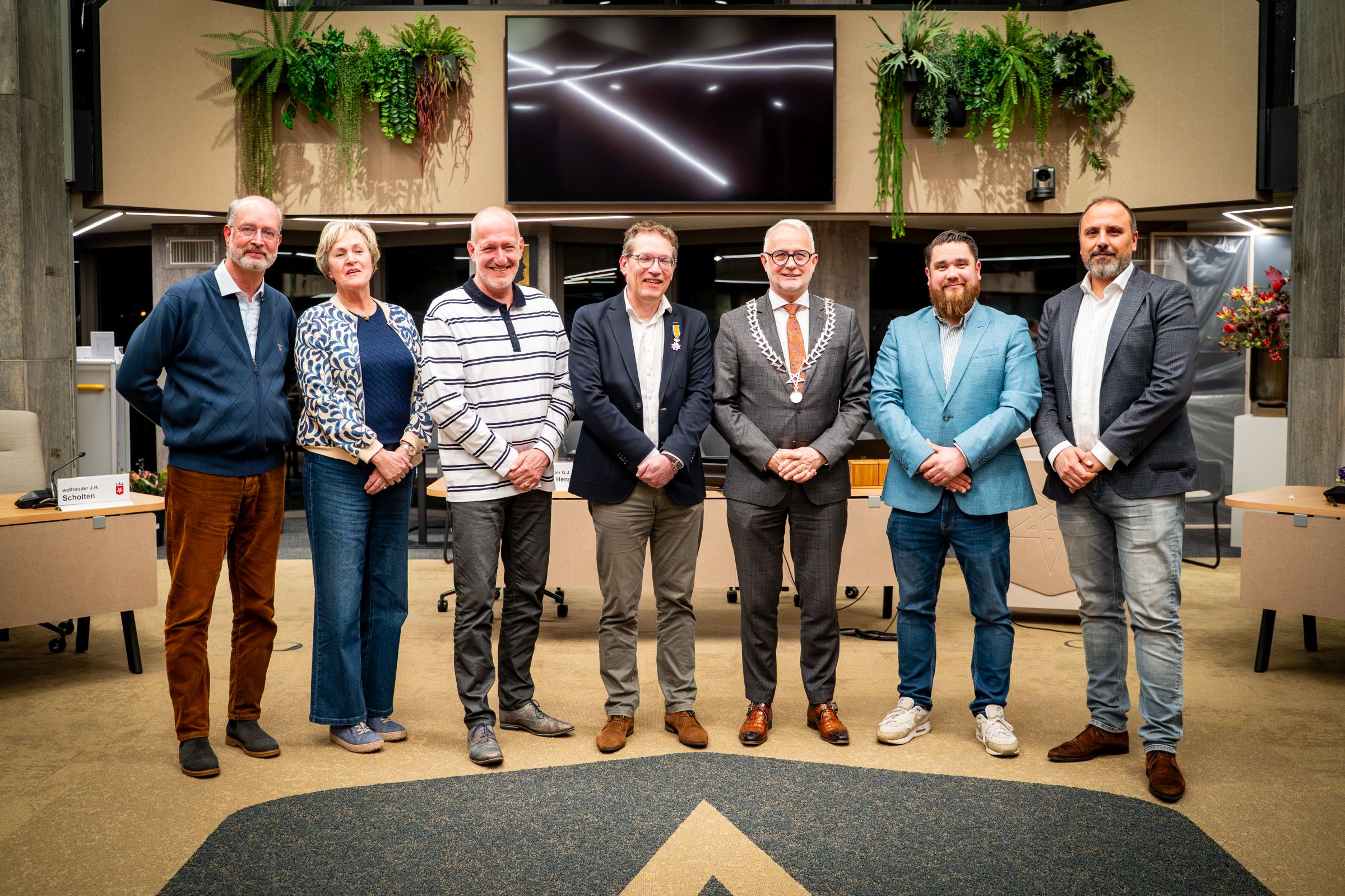 Foto van de zeven vertrekkende raadsleden naast elkaar. Van links naar rechts: Freek Ebeling (VVD), Henriëtte Exterkate-Roerink (CDA), Marco Lassche (TeamDAP), Gert-Jan Vonkeman (D66), burgmeester Gerard van den Hengel, Dario Prinsen (Nieuw Haaksbergen) en Deniz Yüksel (PvdA).  