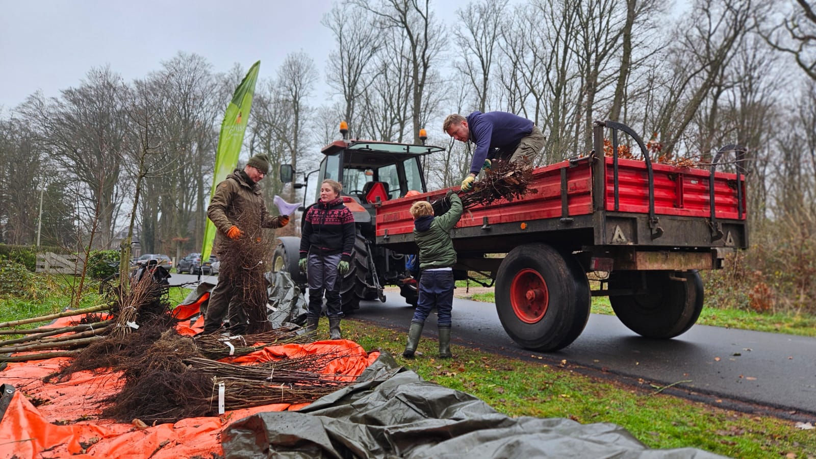 Man deelt bomen uit vanaf de aanhanger achter een tractor. 