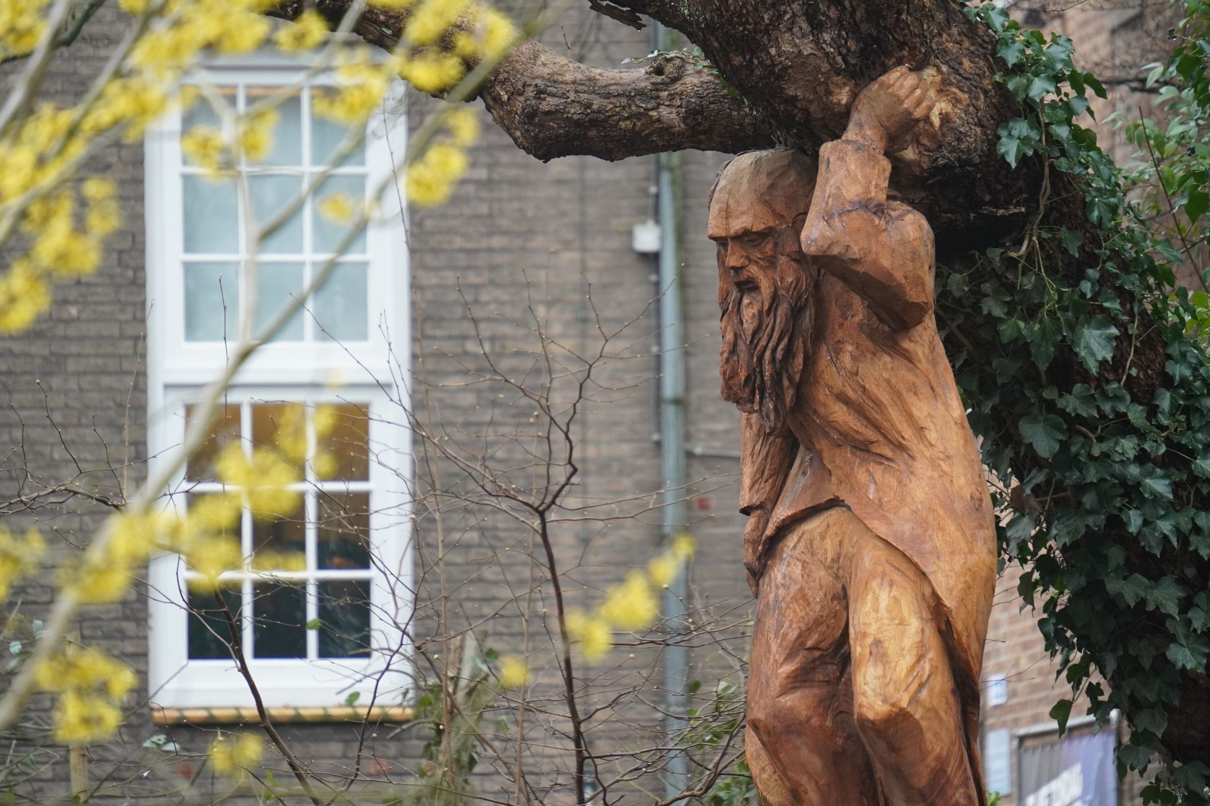 Foto van het houten beeld van Atlas die de trompetboom vasthoudt. 