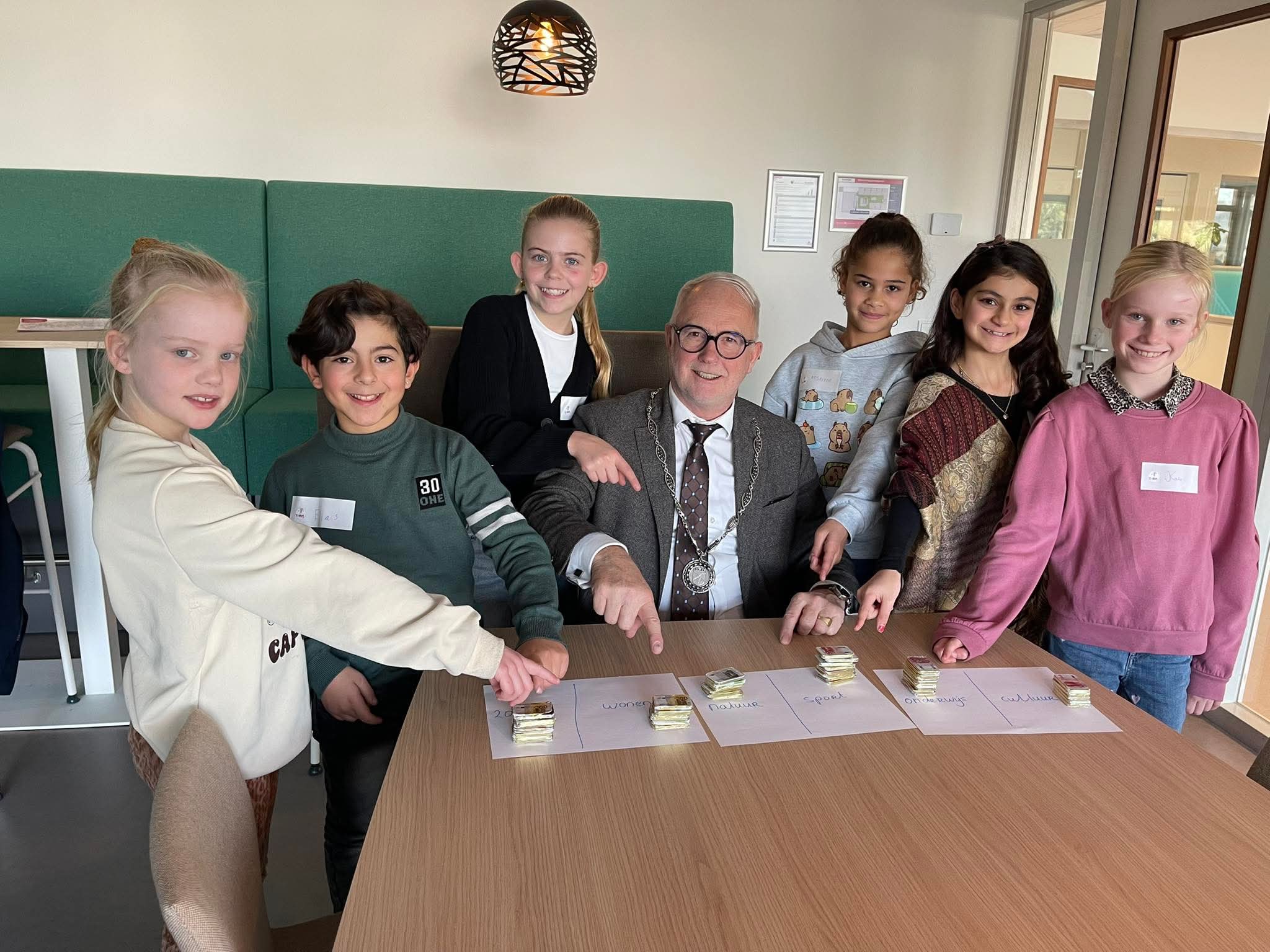 Burgemeester en zes basisschoolleerlingen doen het geldspel.
