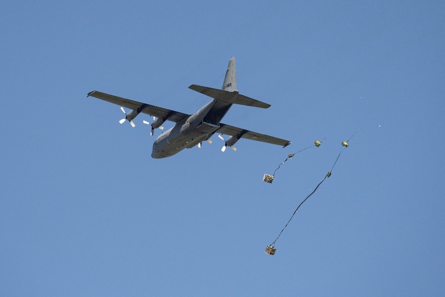 Foto van een c-130 Hercules-transportvliegtuig waar twee pakketjes aan parachutes uit worden gedropt.