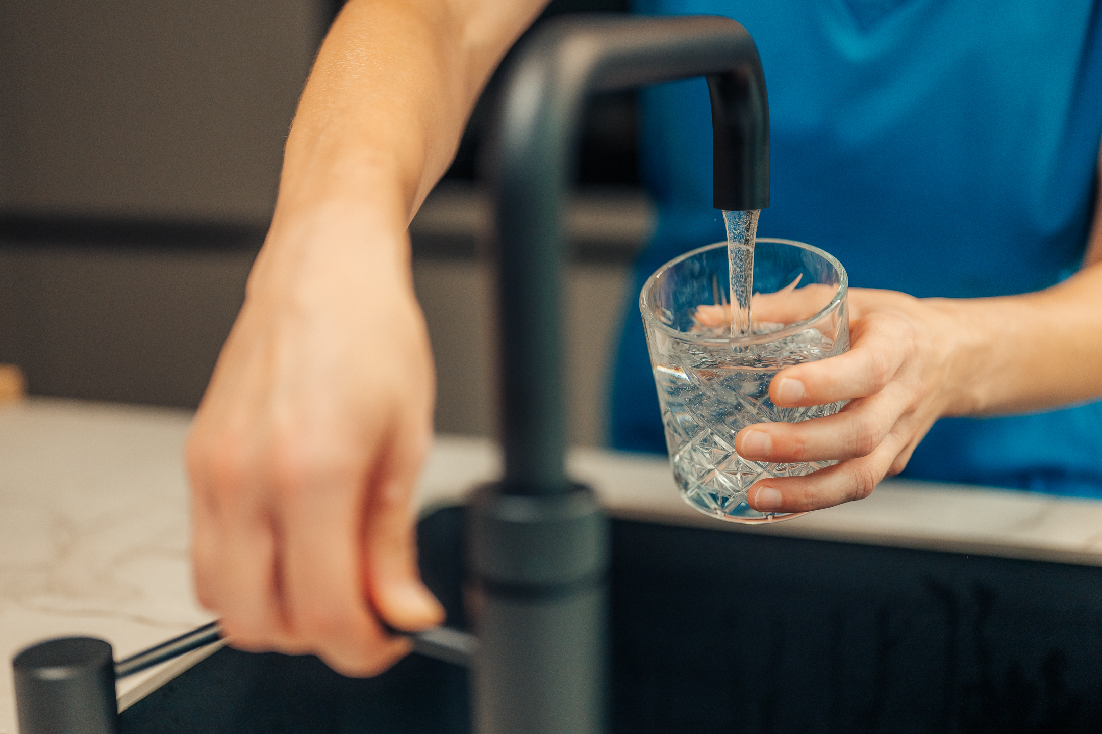 Foto van een drinkglas onder een kraan dat gevuld wordt met water. 