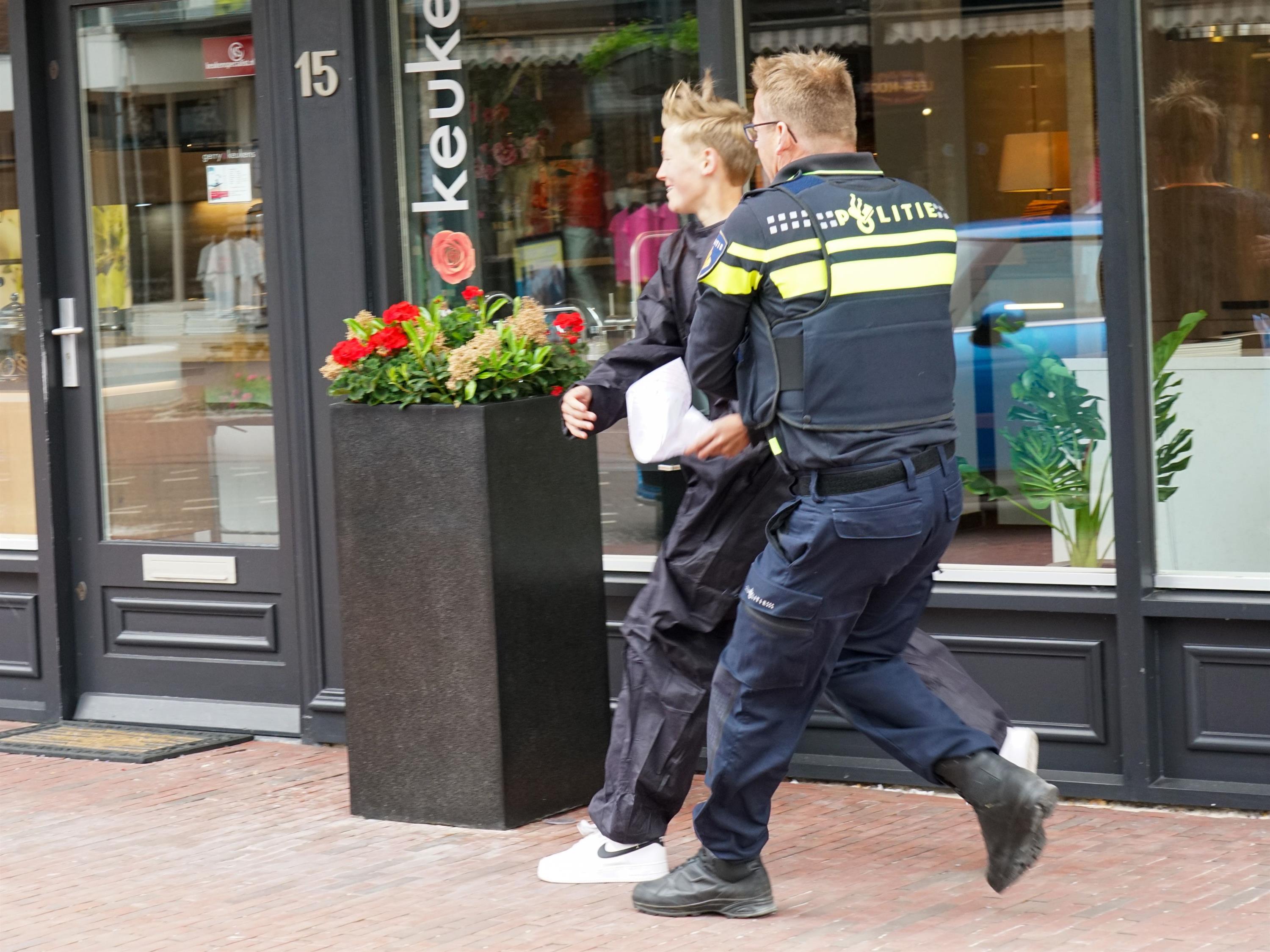 Foto van een jonge deelnemer aan Het Jachtseizoen die getikt wordt door een politieagent in uniform.