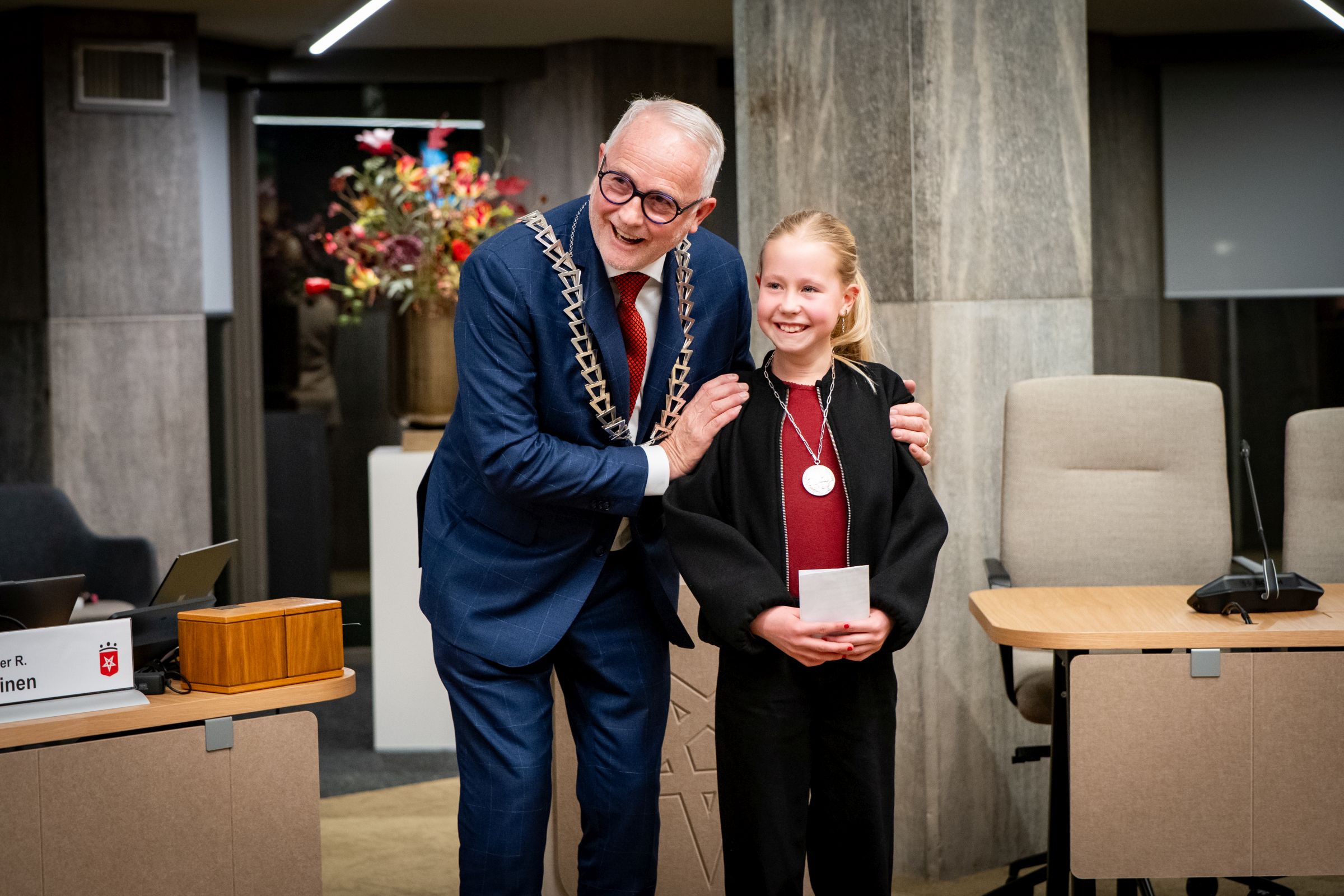 Burgemeester Gerard van den Hengel en kinderburgemeester Janna Winkelhorst staan lachend naast elkaar. 
