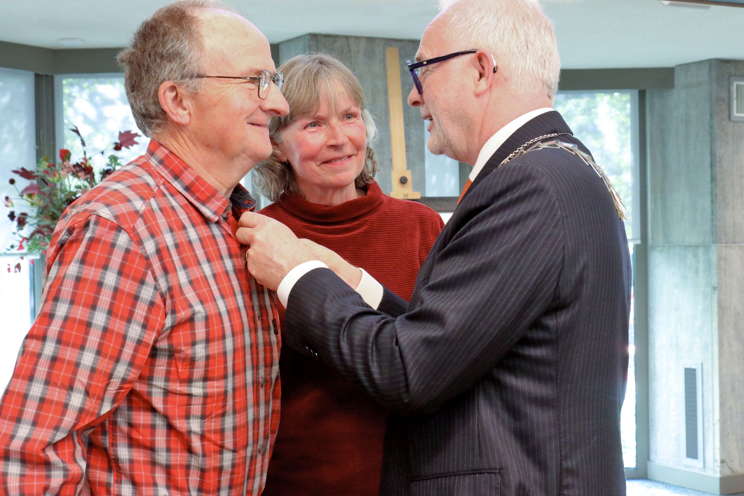 Foto van Henk Westendorp die de onderscheiding opgespeld krijgt door burgemeester Gerard van den Hengel. Mevrouw Westendorp kijkt toe. 
