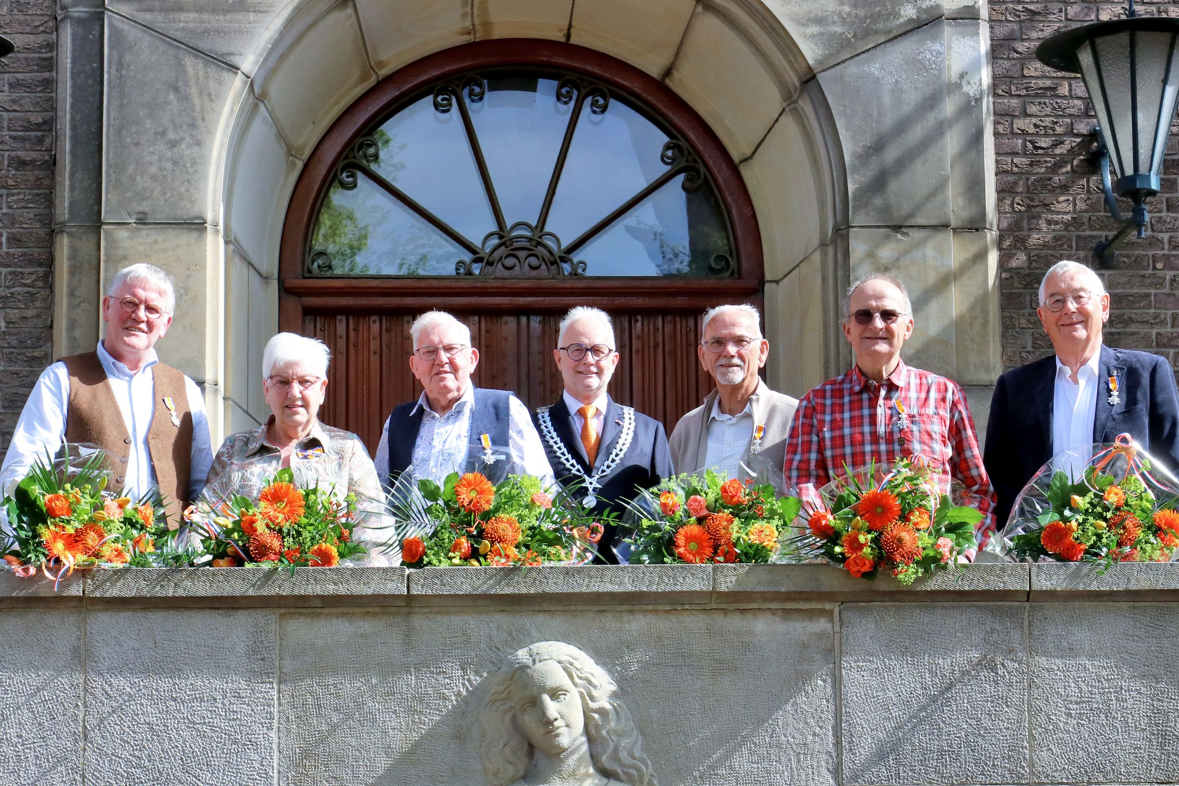 Foto van alle gedecoreerden op een rij op het bordes van het gemeentehuis met burgemeester Gerard van den Hengel in het midden. 
