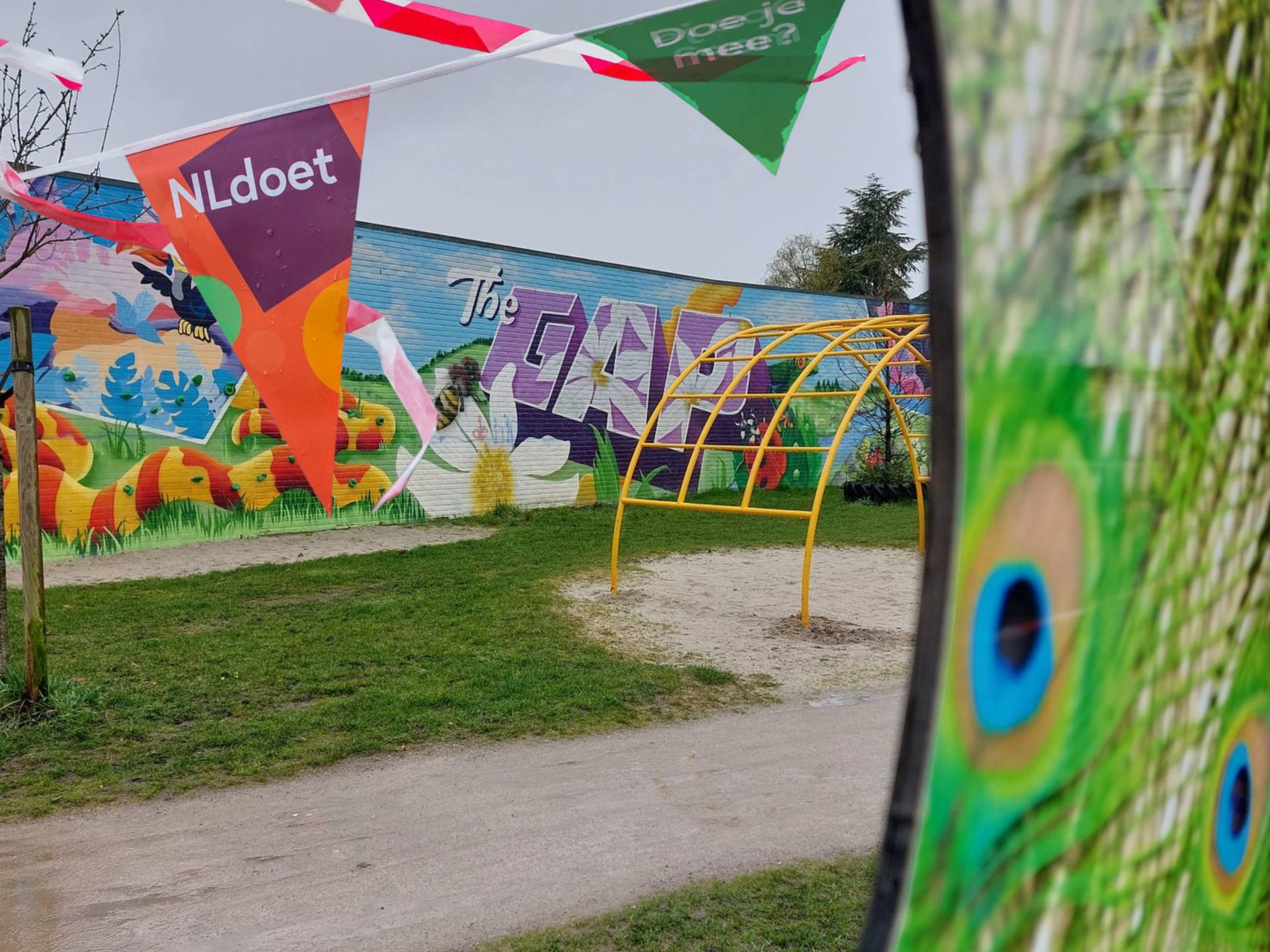 Foto van speelrek en graffitmuur in The Gap met vlaggetjes van NLdoet op de voorgrond. 