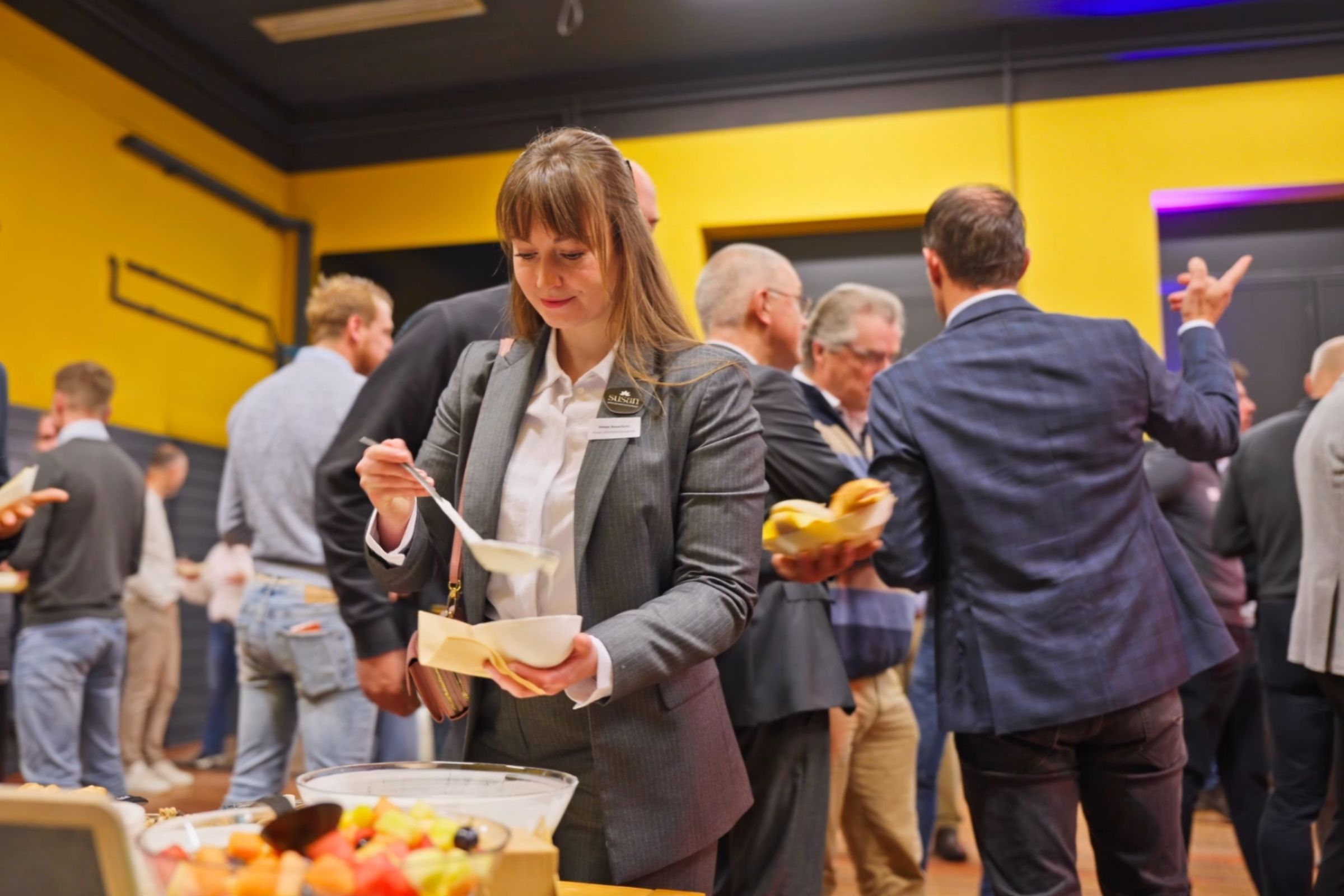 Vrouw schept fruit in een bakje bij ontbijtafel. Op de achtergrond verschillende ondernemers met elkaar in gesprek. 