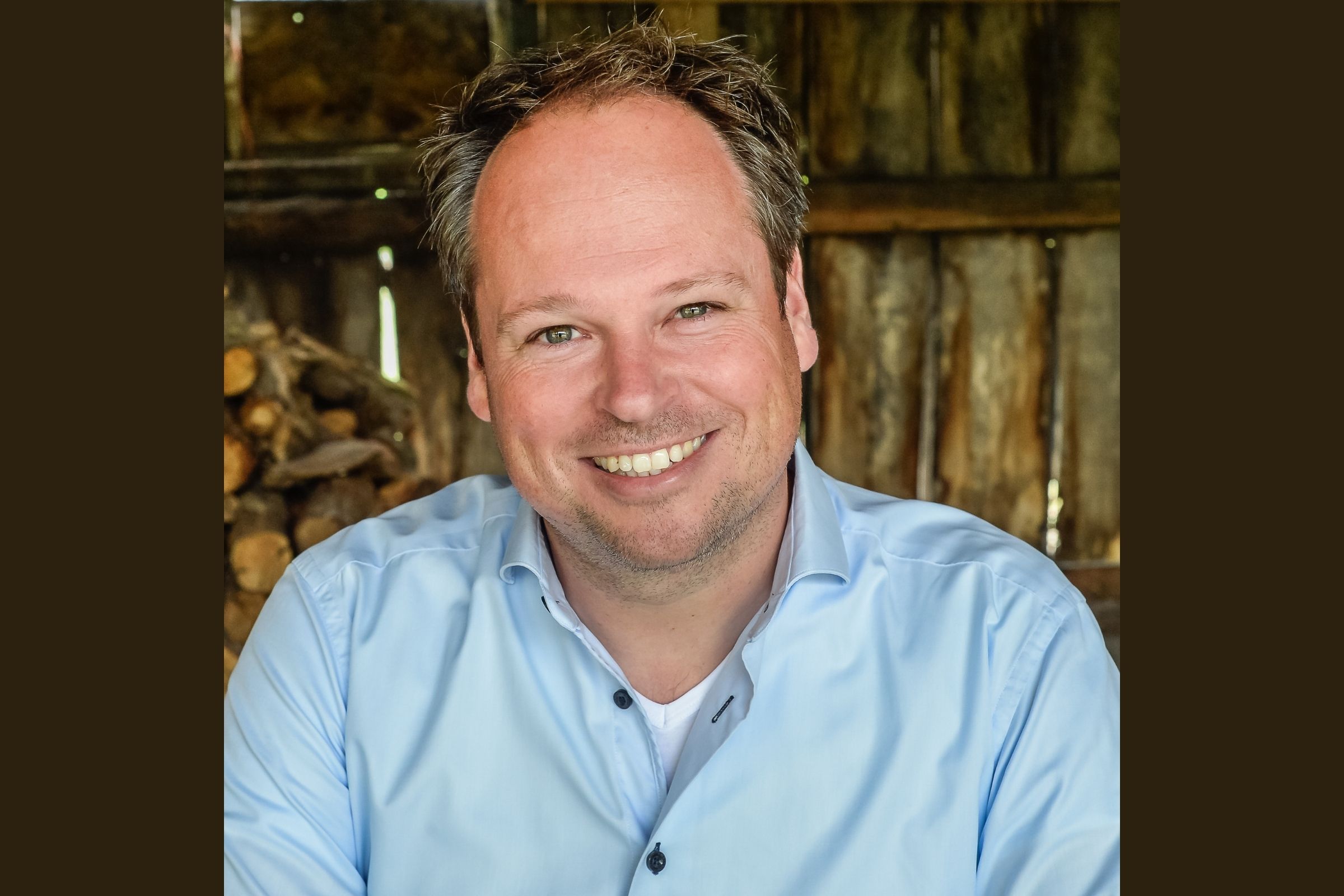 Lachende man met lichtblauwe blouse in houtschuur.