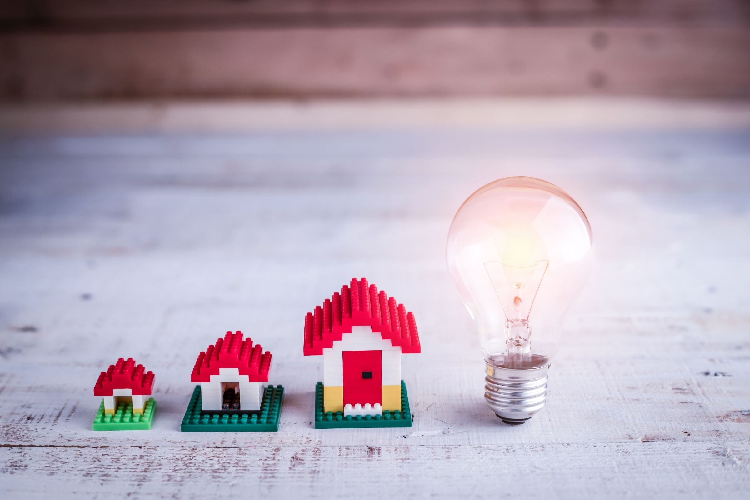 Drie huisjes van lego met een brandende gloeilamp ernaast. 